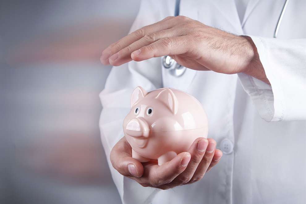 Foto: Arzt hält Hand über Sparschwein
